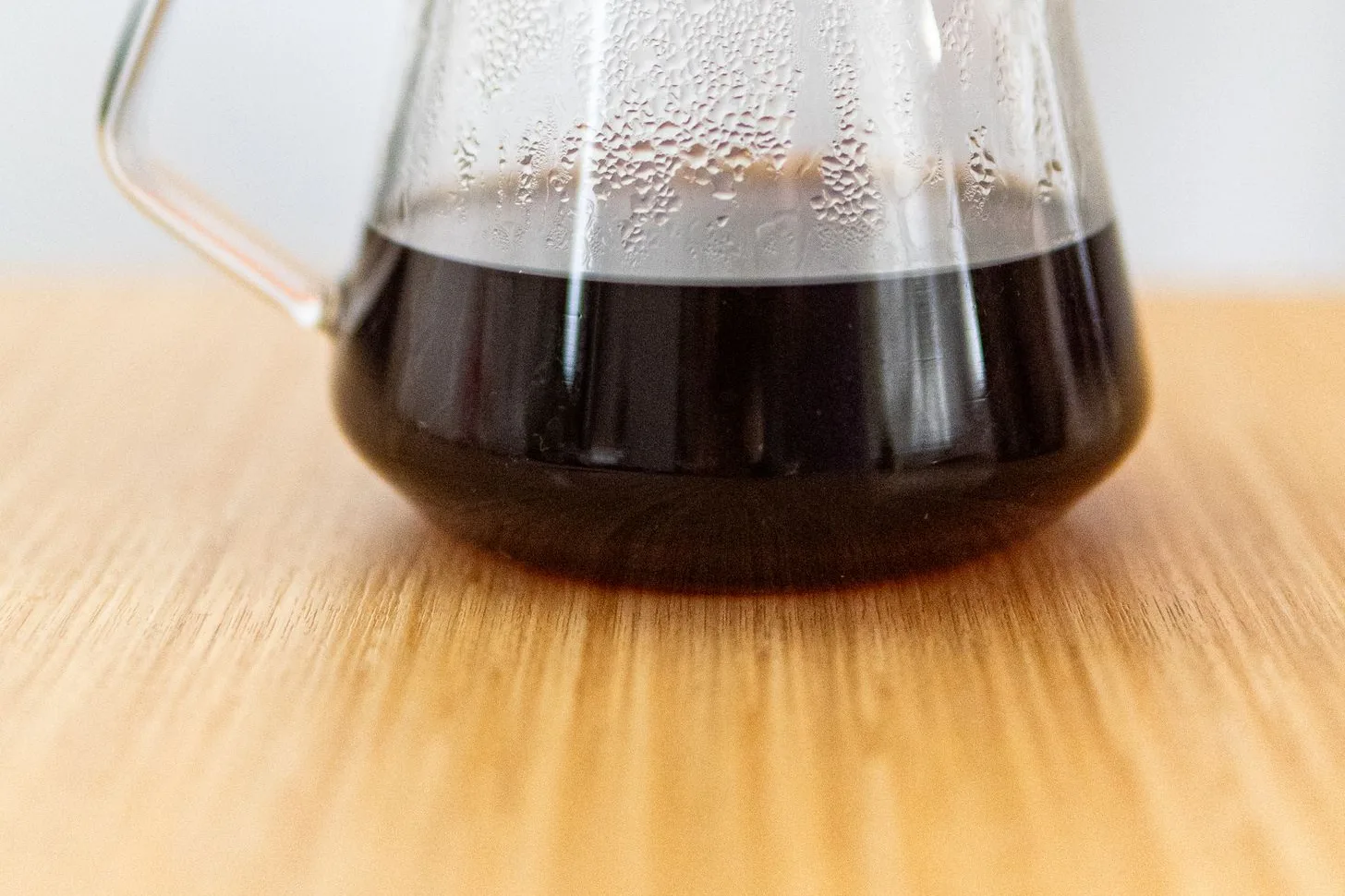 Brewed black coffee in a clear glass server on a wooden table