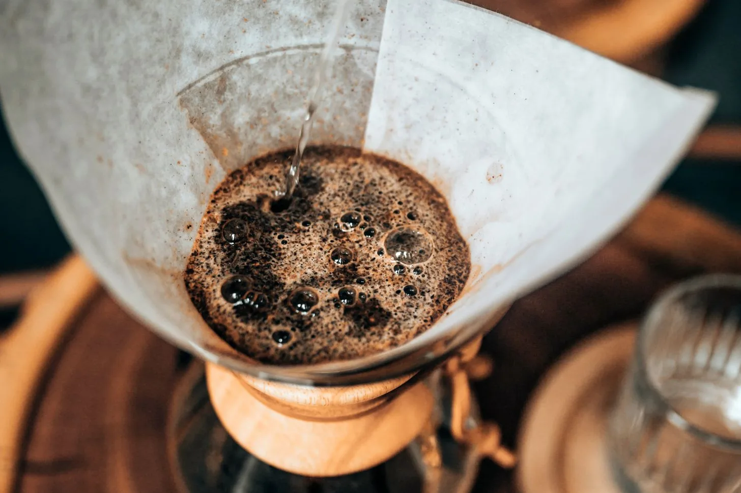 Water pouring onto coffee grounds in a paper-lined glass brewer