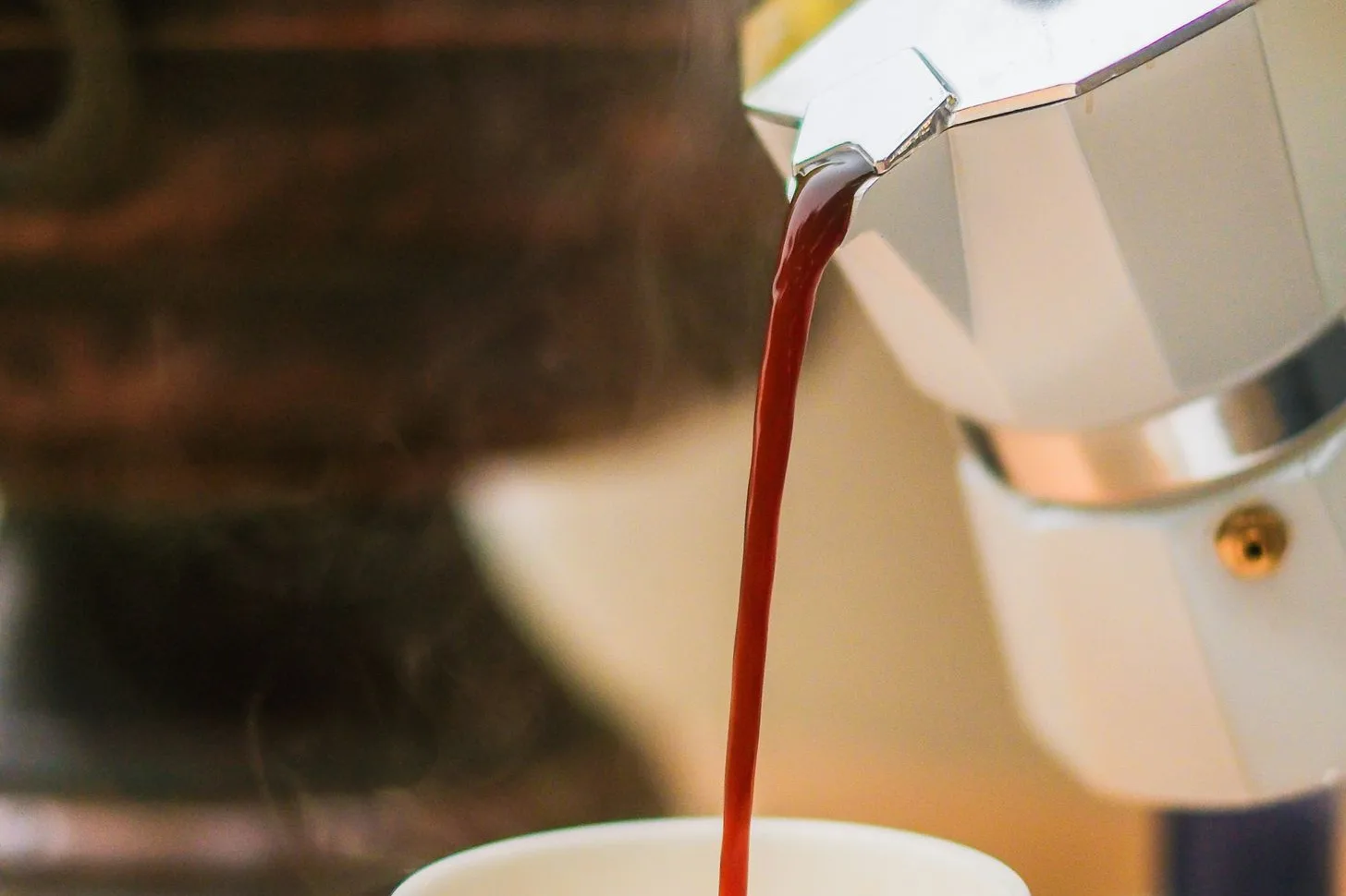 Coffee pouring from a pale moka pot into a white mug