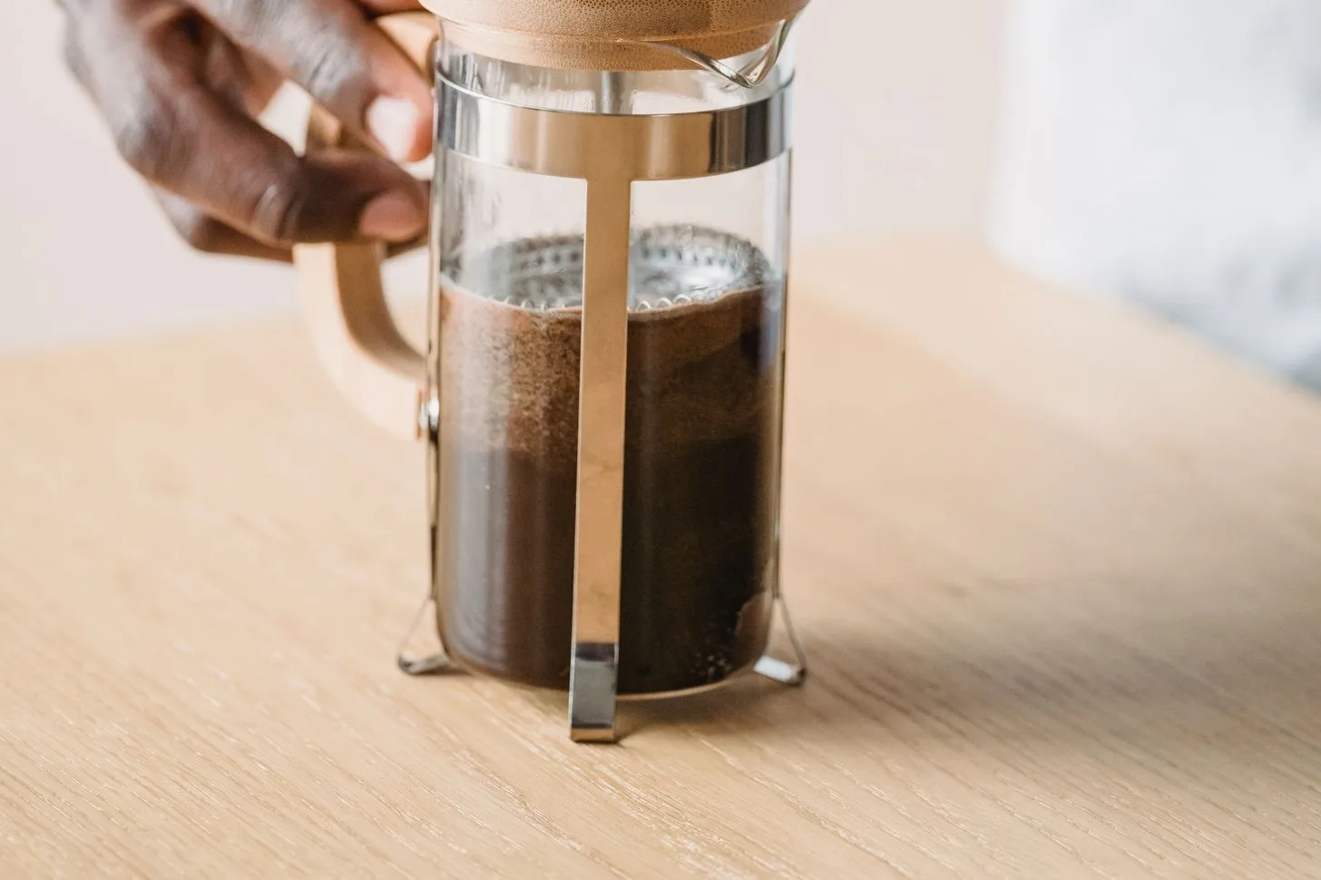 A hand steadying a glass French press on a wooden counter